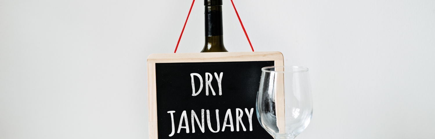 Picture of an empty wine bottle holding a Dry January sign next to an empty win glass.