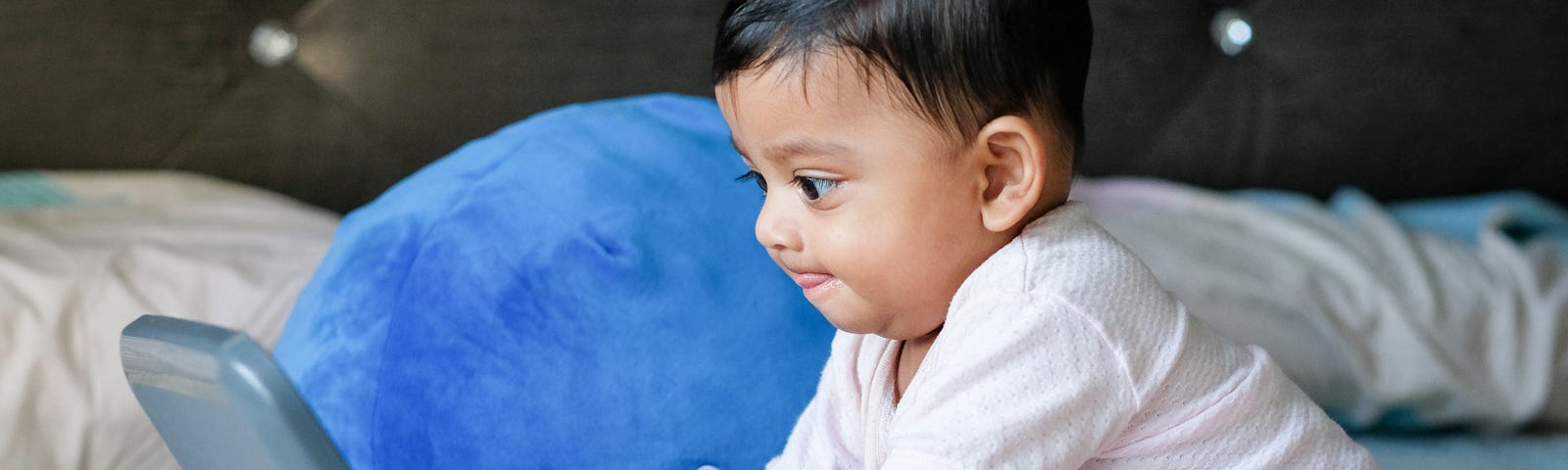 A baby staring intently at a screen with hands on a keyboard