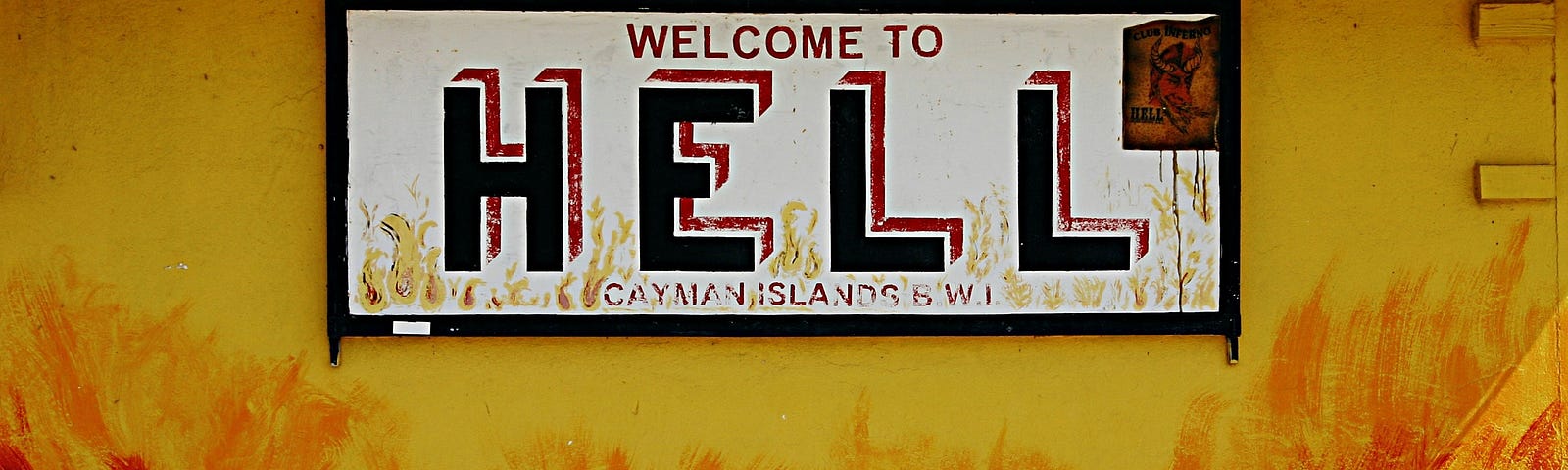 A sign reading “Welcome To Hell, Cayman Islands” hanging on a wall coloured like it is set aflame.
