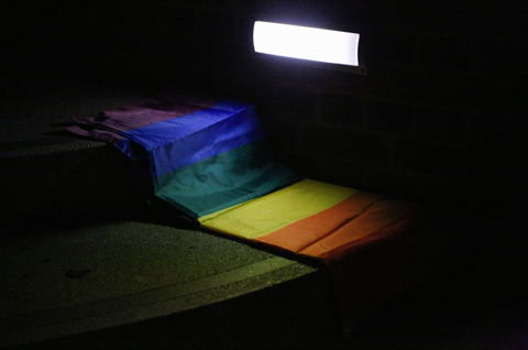 A rainbow banner sits in darkness with a small window shining light on it
