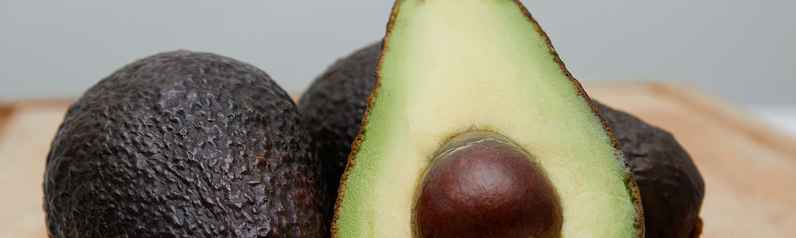 avocado sliced open, with two avocados unopened behind it