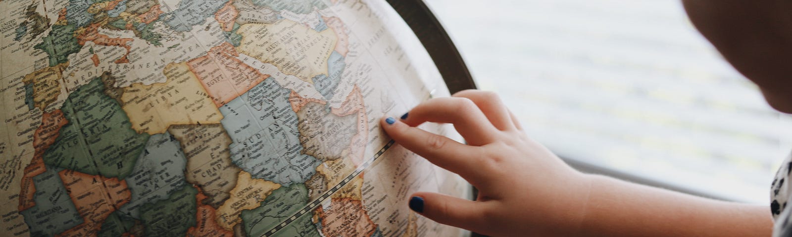 A person touches a globe that is sitting on a desk. The piece is about learning from a foreign culture. The globe represents the smallness of the world which ties into a central theme of the piece, that people around the world share many common traits.