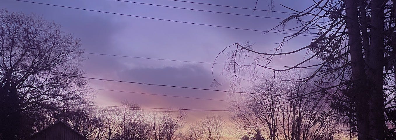 Sunrise photo taken with a cell phone. Silhouetted shapes of trees, power lines, a fence, and a barn set beneath or against a purplish sky with rising pink-gold light and soft clouds.