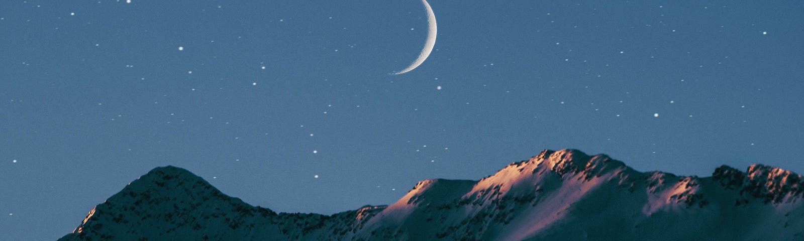 The new moon in a star filled sky over snow touched mountain peaks