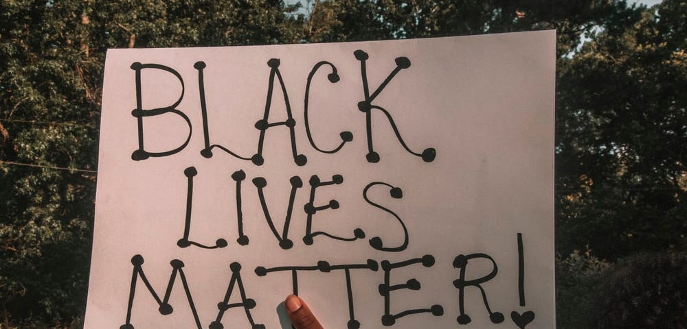 A hand holding a poster which says “Black Lives Matter”