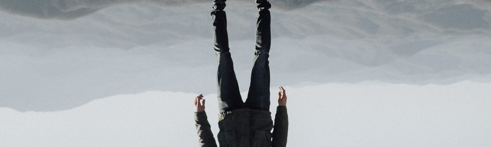Upside down photo of a man dressed in black floating above mountains