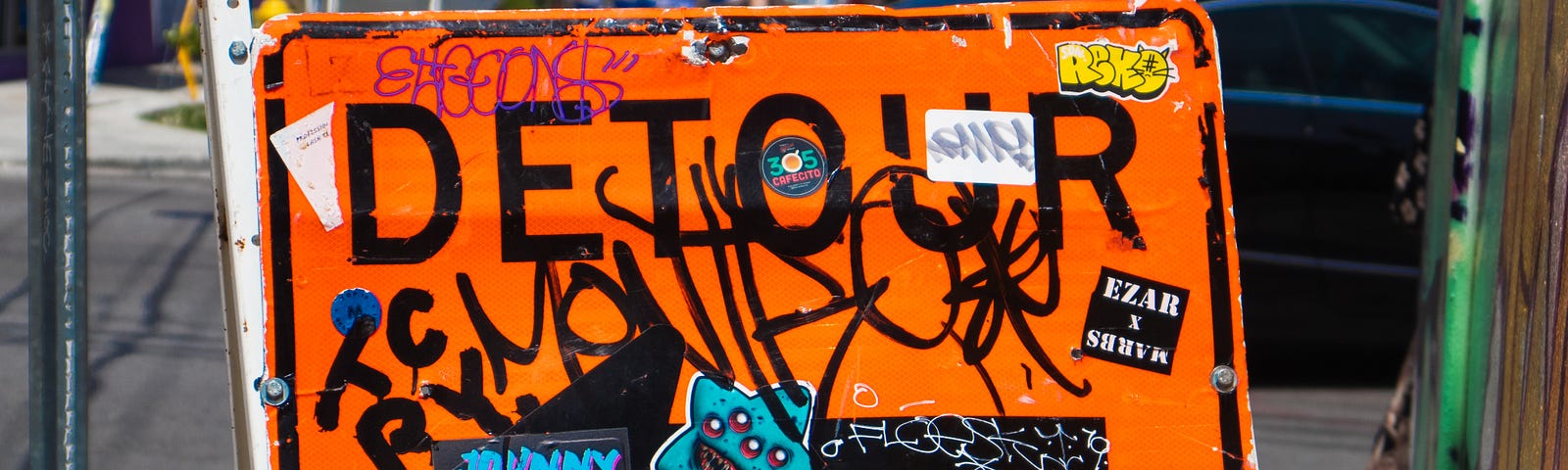 A close up of an orange detour sign with a left pointing arrow and graffiti on it.