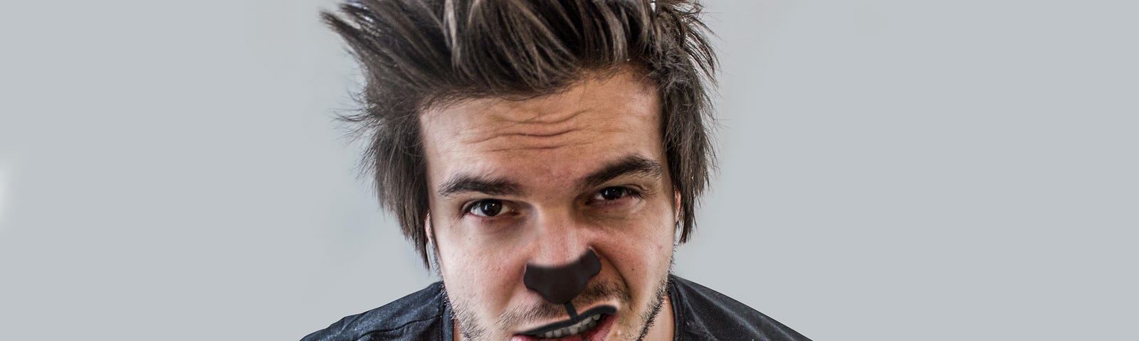 A young man dressed in a bear head tie and bear nose. He is wearing a T-shirt. He is also looking haggard and crazy.