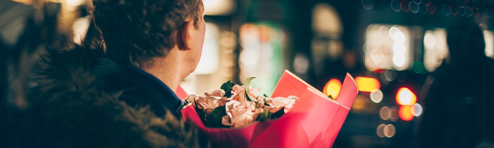 A man holding flowers waiting for someone to arrive.