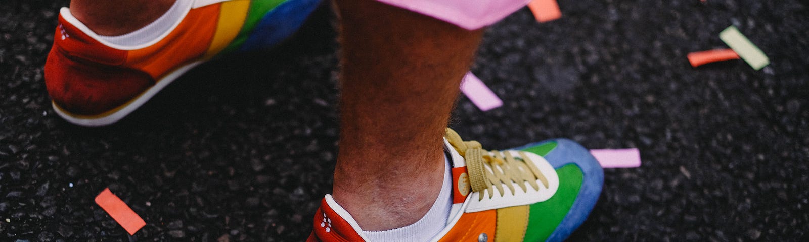 Someone’s feet in rainbow shoes with many colors of confetti on the ground