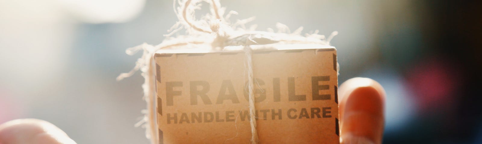 A small box which says “FRAGILE: handle with care” is wrapped in string and sits in the palm of a hand.