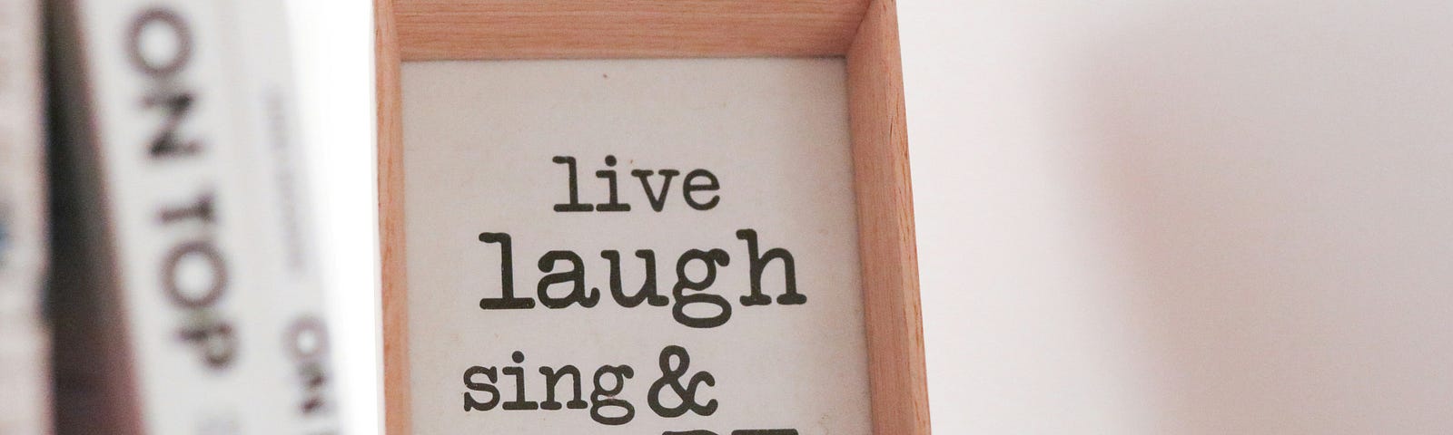 A white sign surround by a small wooden frame saying, “Live Laugh Sing & Be Happy.”
