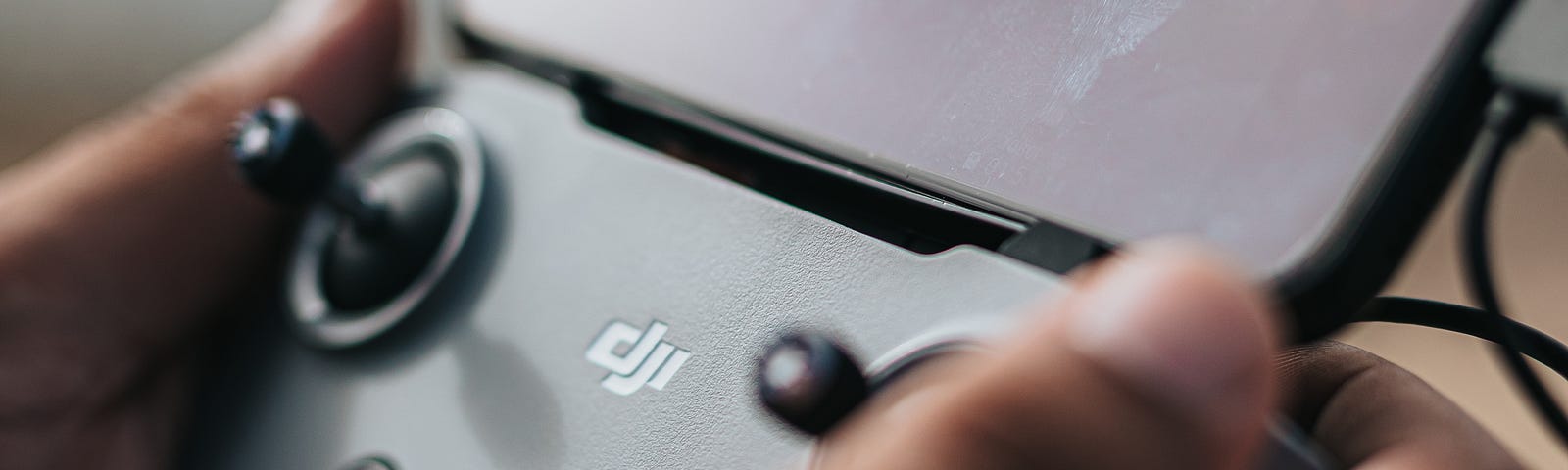 A hand grasping either side of a controller (in this case one that uses a smartphone attached to a dji controller console).