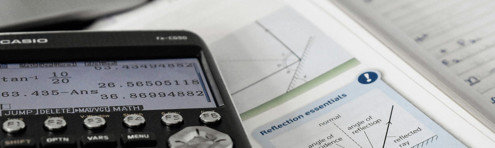 A calculator on the textbook and next to a laptop.