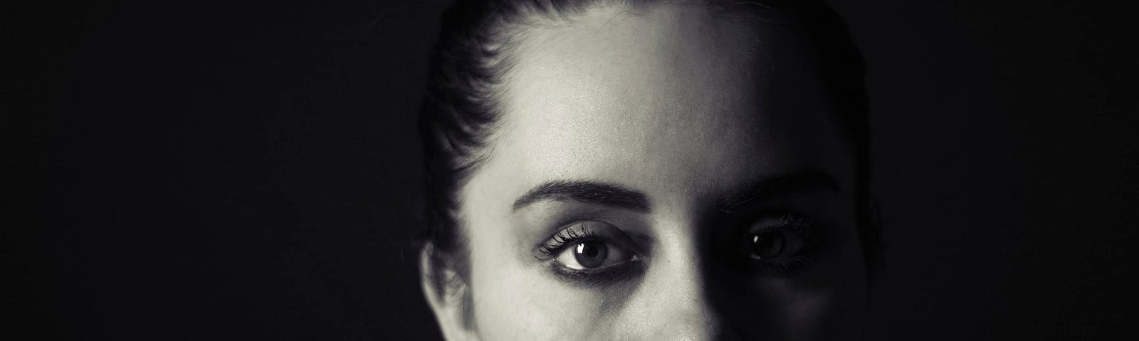 Black and white photo of a shadowed young woman with a tear stream down her face, running her dark eye makeup.