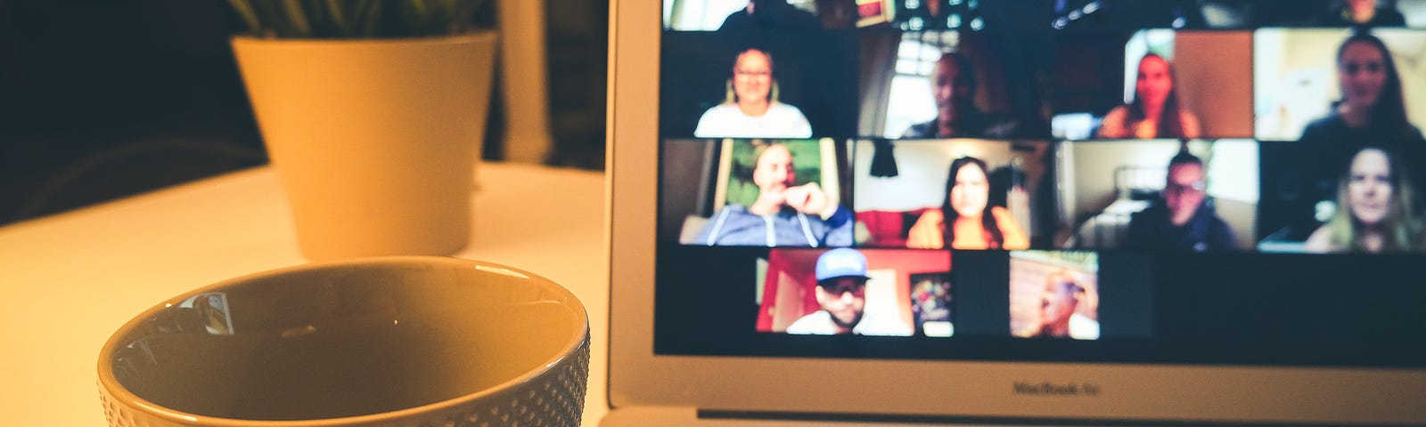 A photo of a laptop, open to show an online meeting, with a cup by its side.