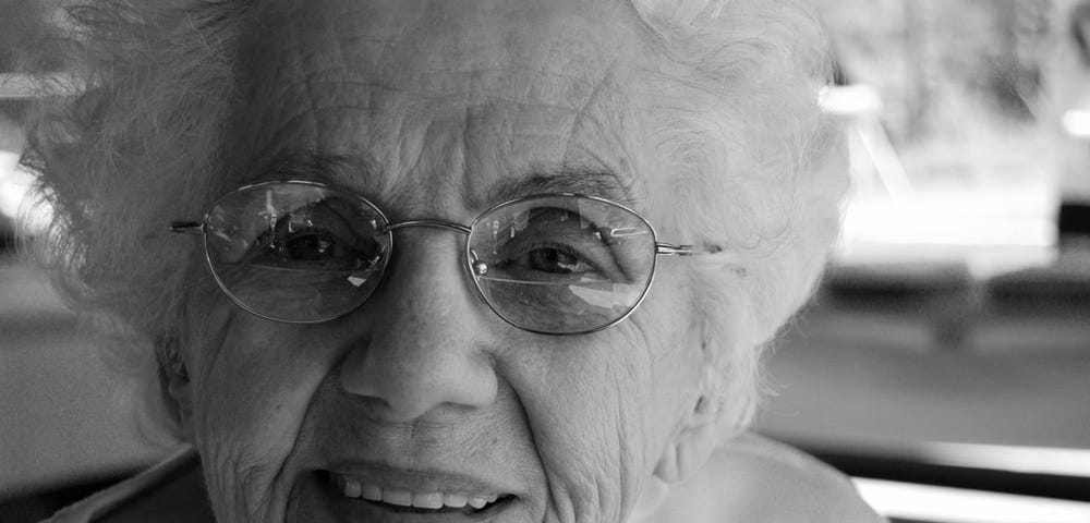 A senior lady wearing glasses, smiling.