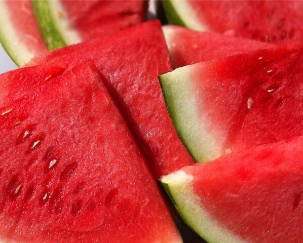 A photograph of large triangle shaped slices of watermelon on a white surface.