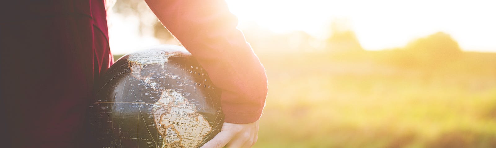 A person holding a globe in a sunny field.