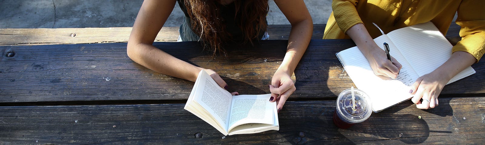 overhead view of three people sitting at a picnic table reading and writing in books and journals