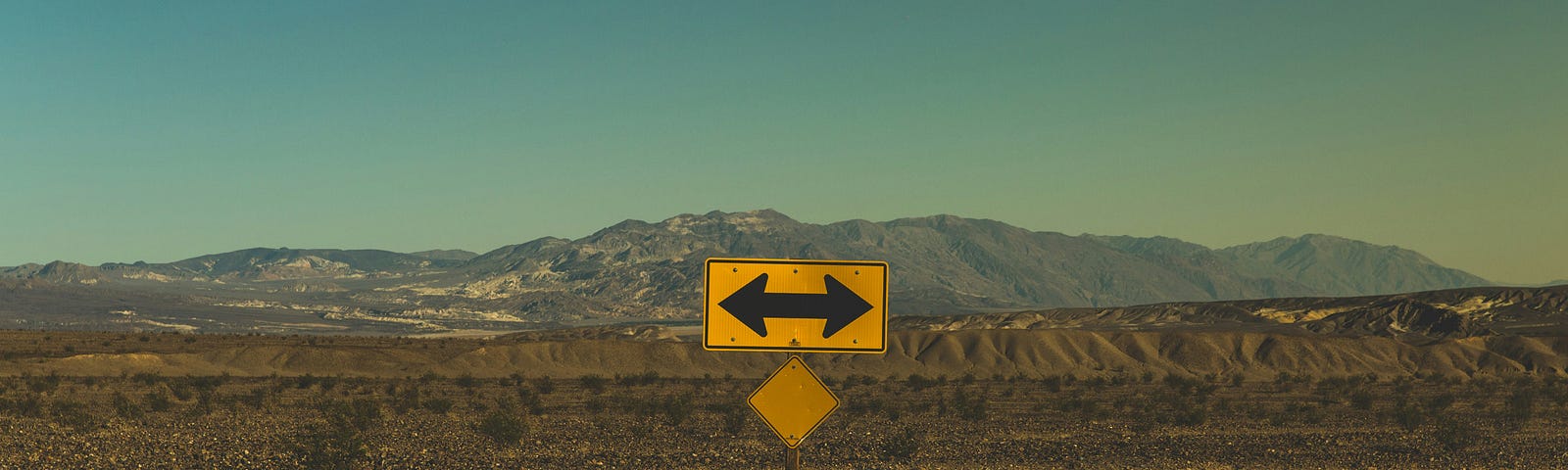 Double tipped arrow sign at T intersection, in desert. No informative labels anywhere.