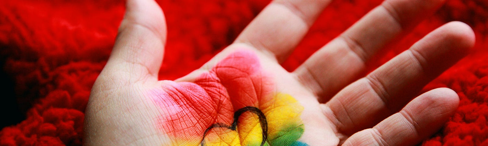 A hand with the rainbow flag painted. A heart is drawn in the centre