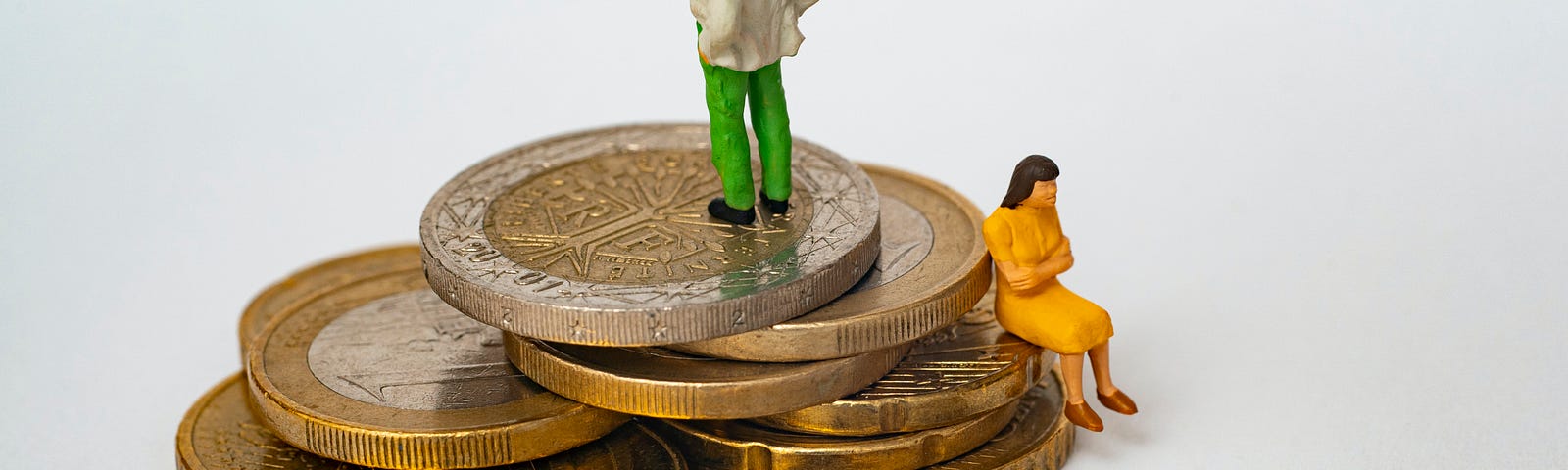 Stack of coins with two ceramic figurines. One of a man standing on top of the stack and another of a woman sitting down on the “ledge” of a coin.