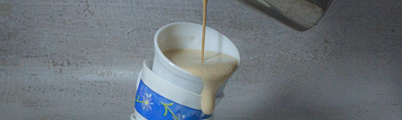 a metal pitcher spilling a drink into a coffee-cup tower