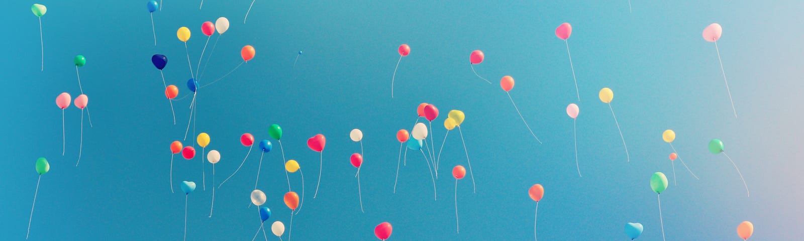 A true flock of multicolored balloons floating into a blue sky.