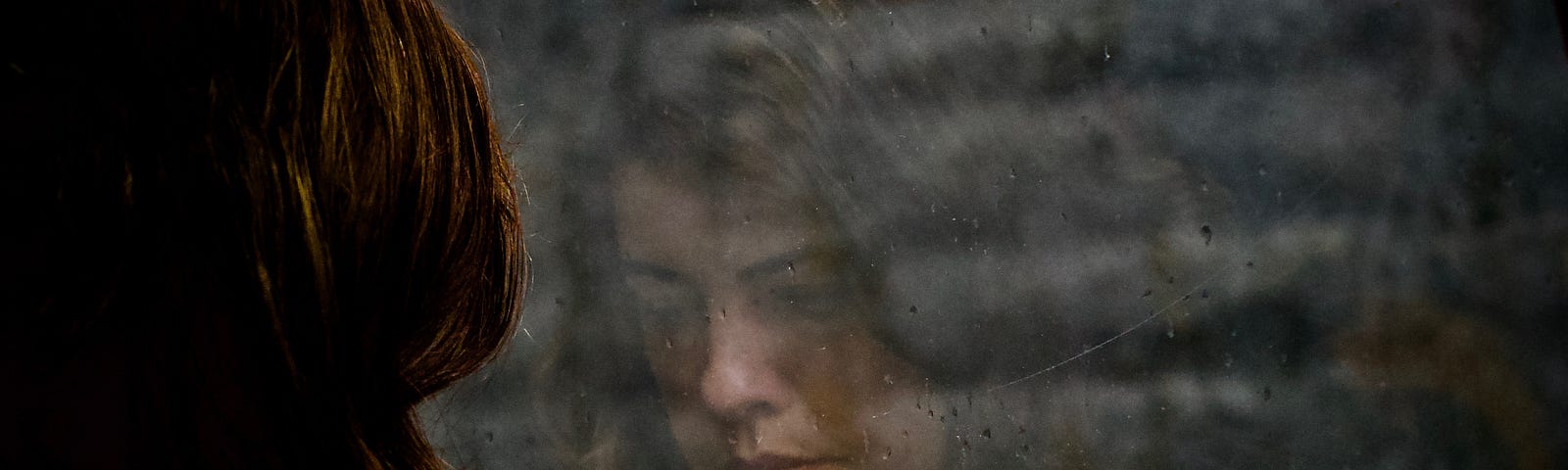 a sad woman’s face reflected in a dark brick wall