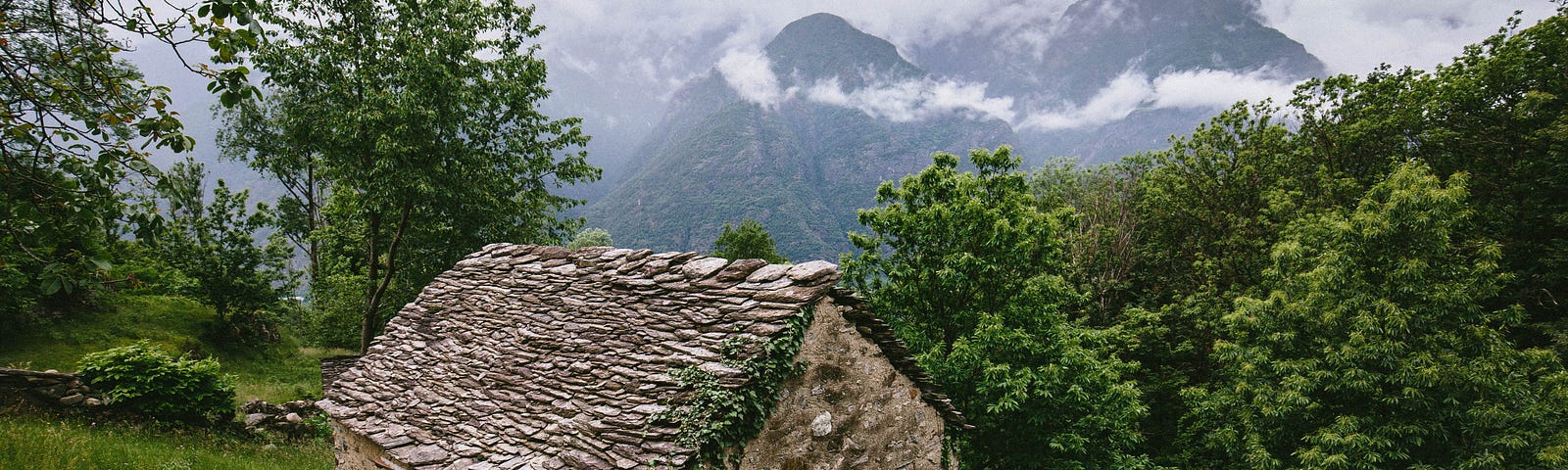 A stone hut in the side of a hill surrounded by green nature.