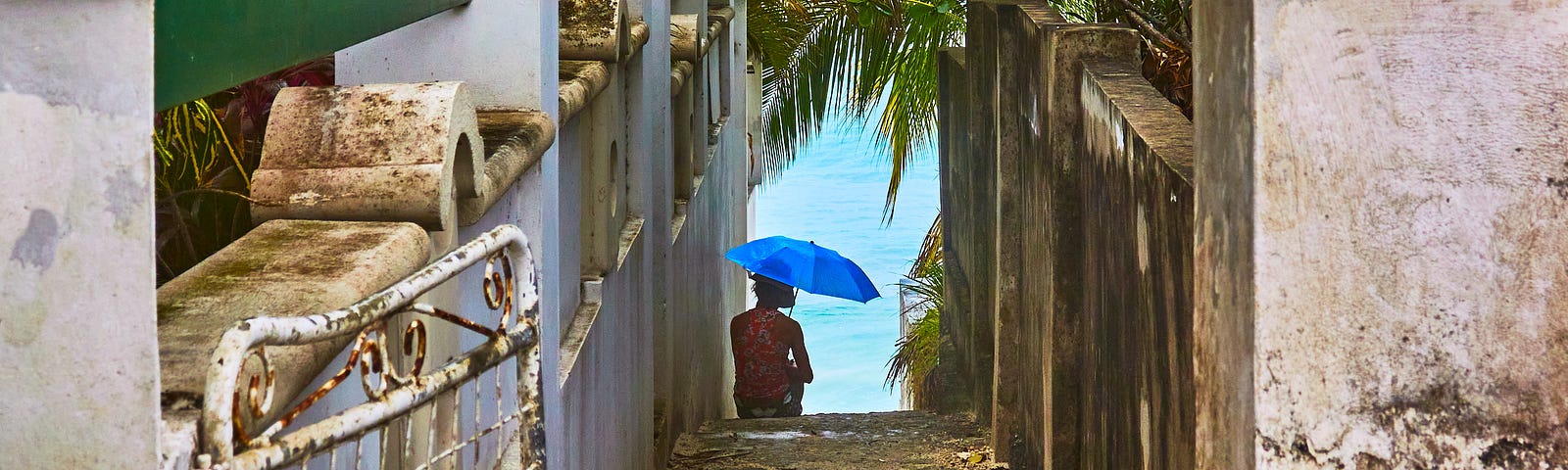 Woman with an umbrella sitting in a narrow alley leading to the beach in Barbados