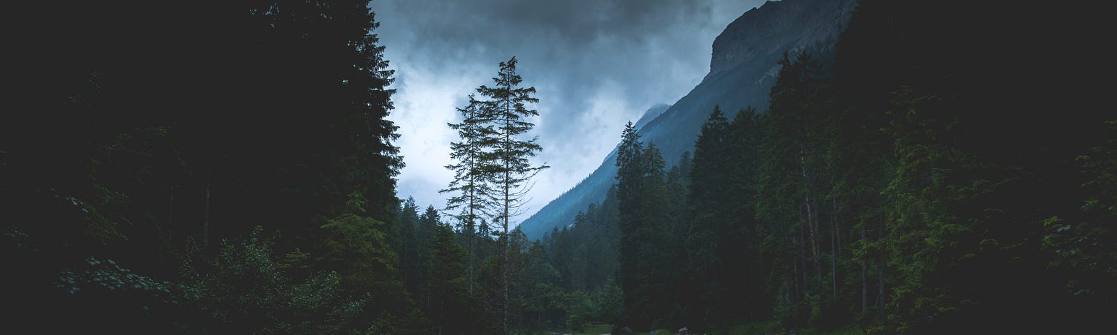 A beautiful photograph of a valley in between two mountains with a streak snaking through it. The sky is dark with storm clouds.
