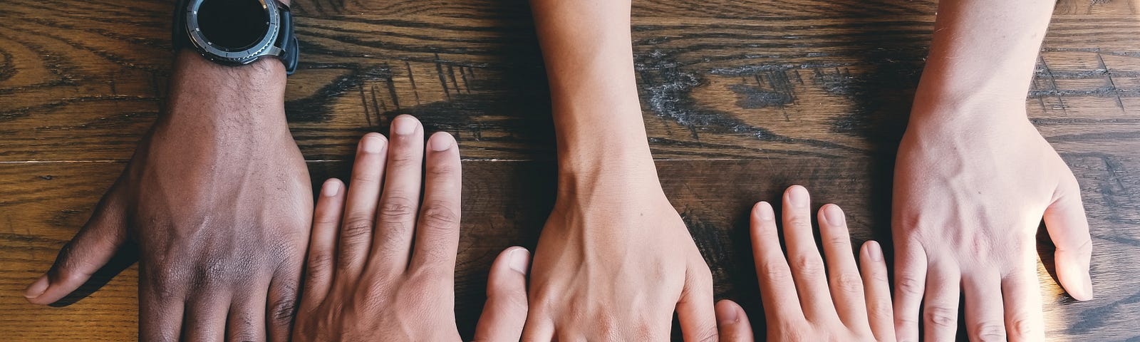 Picture of a wooden table with four peoples’ hands on side by side.