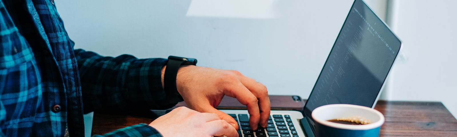 Someone typing on a laptop, with a cup of coffee.