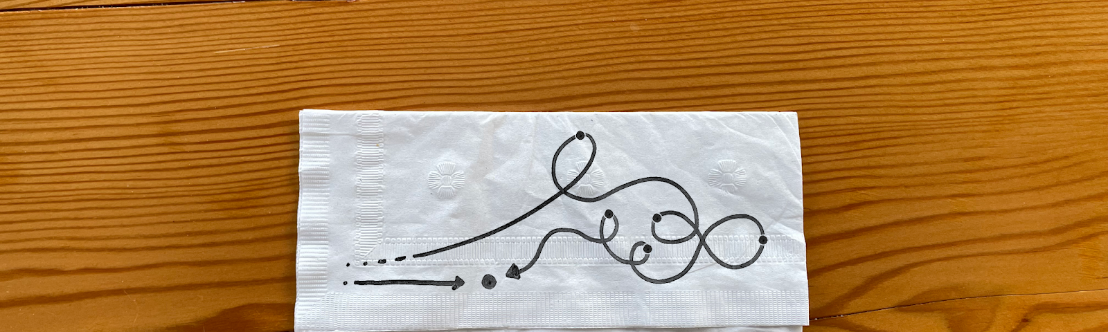 White napkin with a black ink line drawing. One arrow points straight at a dot. The other arrow takes a squiggly path to get to the same dot.