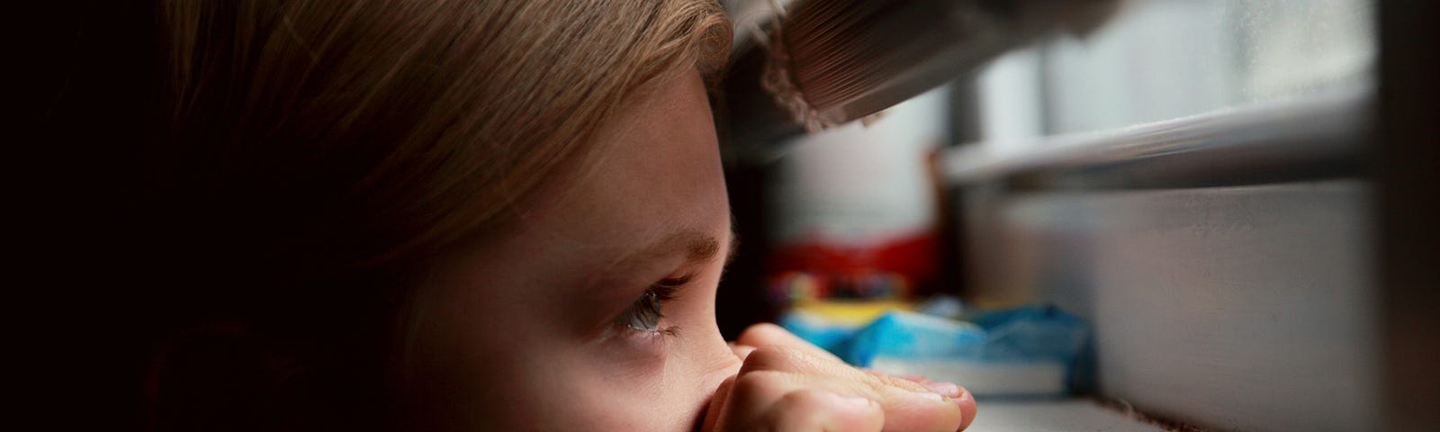 Here is a photo of an innocent child, peering through a window slit fearfully, fearing something, possibly feeling abandoned and hopeless.