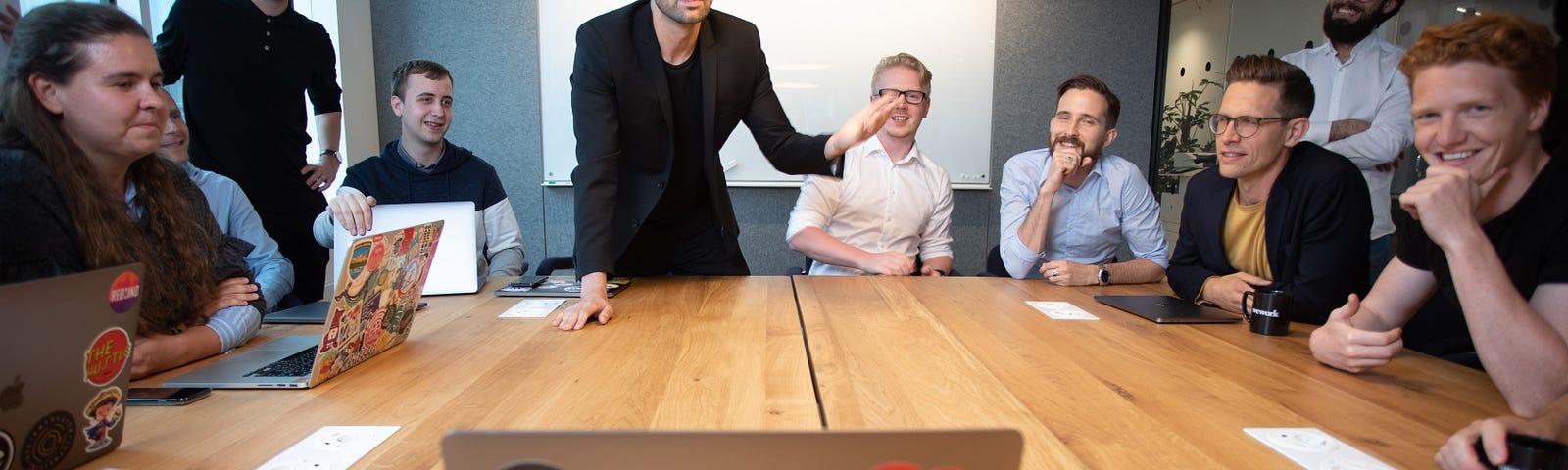 People gathered around a conference table, there is a speaker leaning in toward the group.