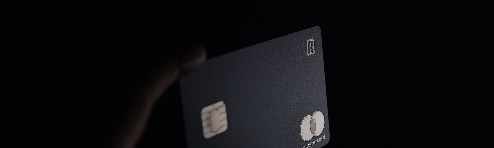 A hand holds a credit card up against a black background.