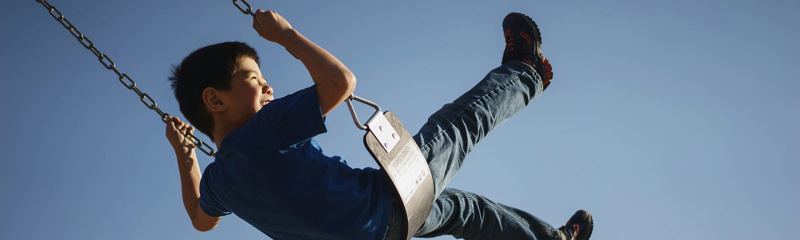 a boy in a blue shirt swinging on a park swing with his legs in the air