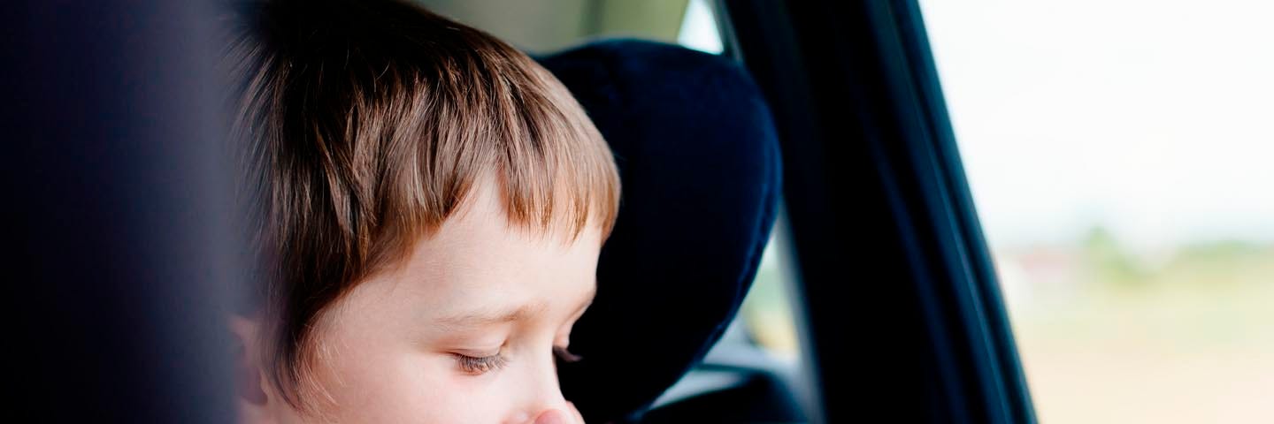 A child sitting in a car facing the window and covering his mouth. He looks ot have carsickness.