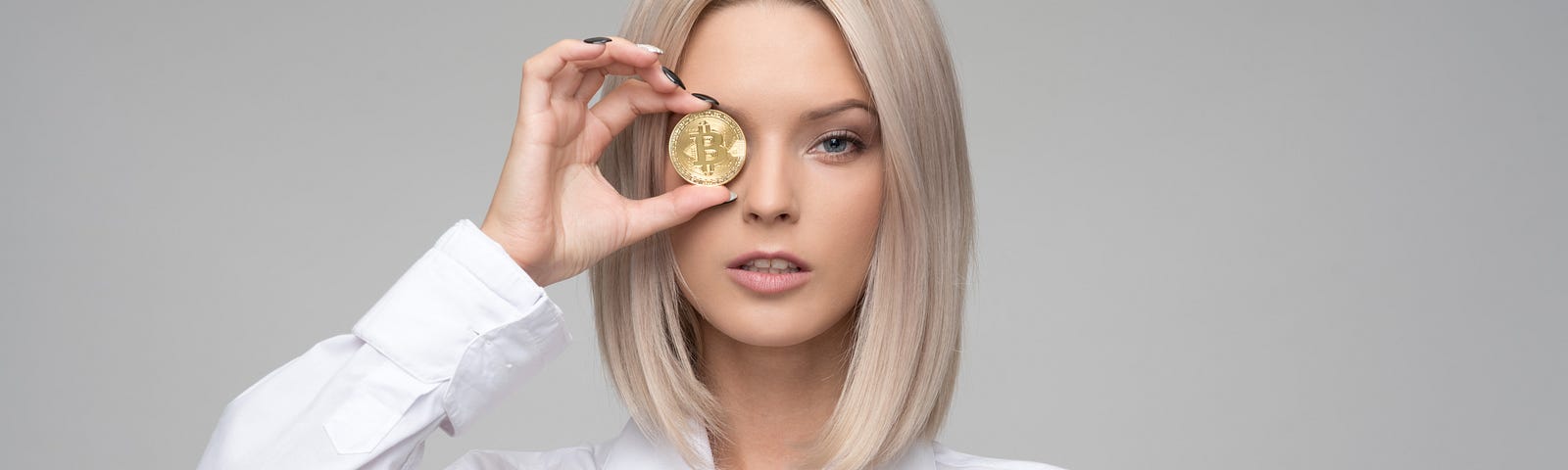 Blonde woman holding gold coin to her eye.