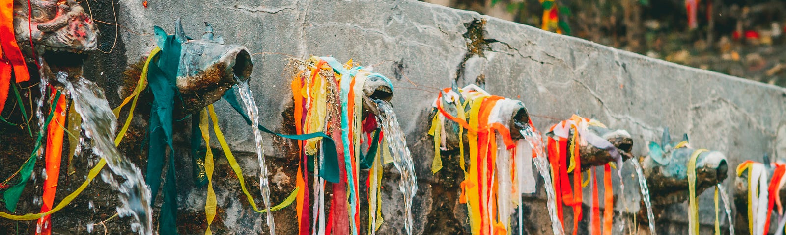 pipes sticking out of a wall have colored cloth and string hanging from them.