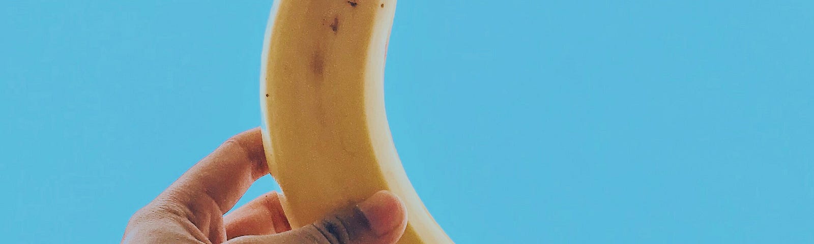 A picture showing a hand dolding a banana. As a background the blue sky.