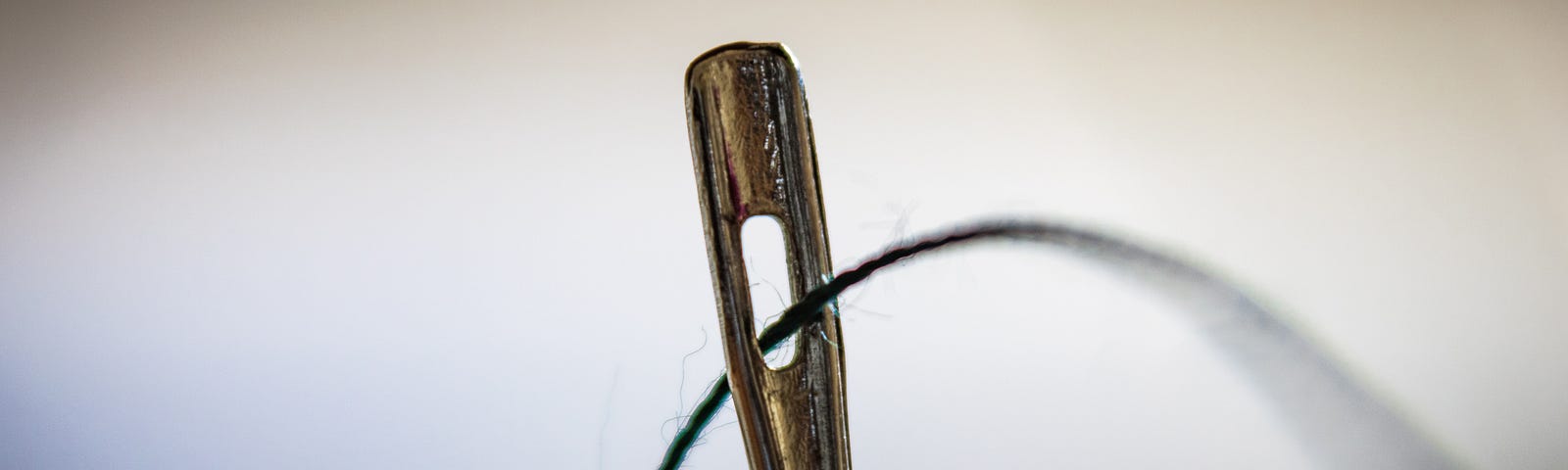 Close up of black thread through the eye of a needle