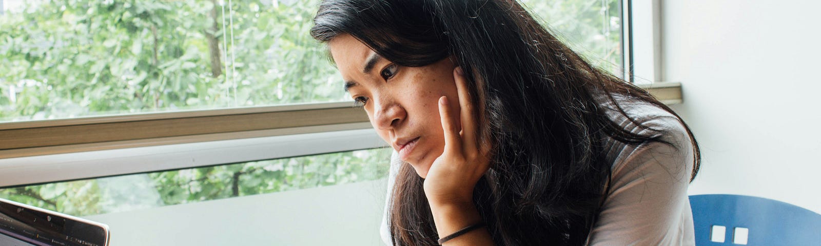 An attractive woman stares at laptop in an office setting.