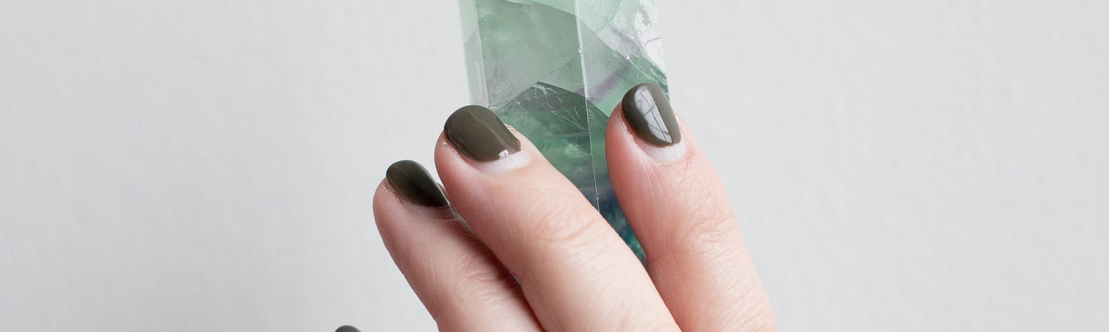 Woman’s hand holding a green crystal representing the use of crystals to attract money.