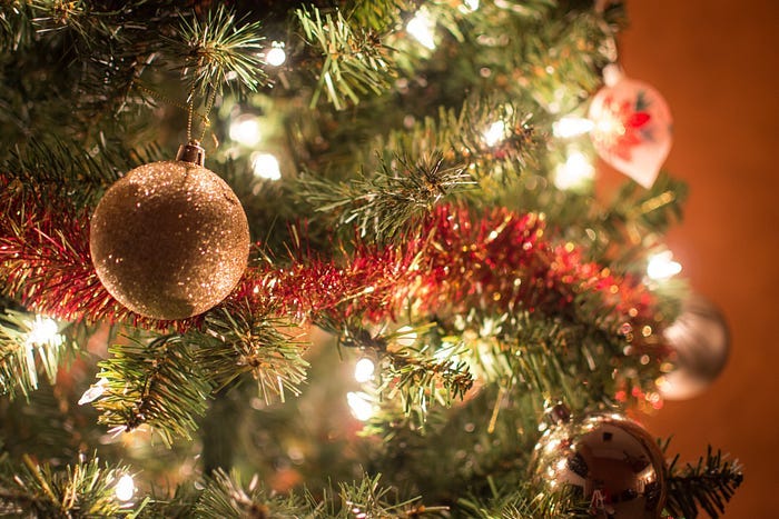 Close up of golden ornaments and red garlands on a lighted Christmas tree.