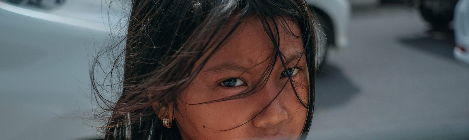 A child in the street, approaching a car window — looking at you with a sad but hopeful view in her eyes