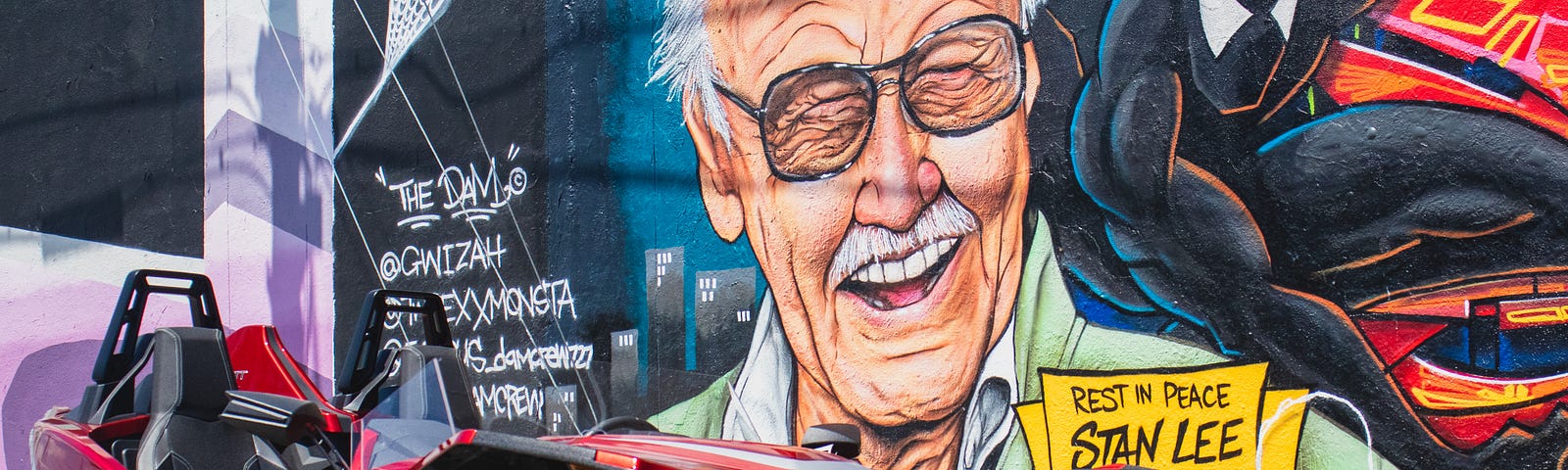 A wall mural of Stan Lee and Spider-Man behind a souped-up car.